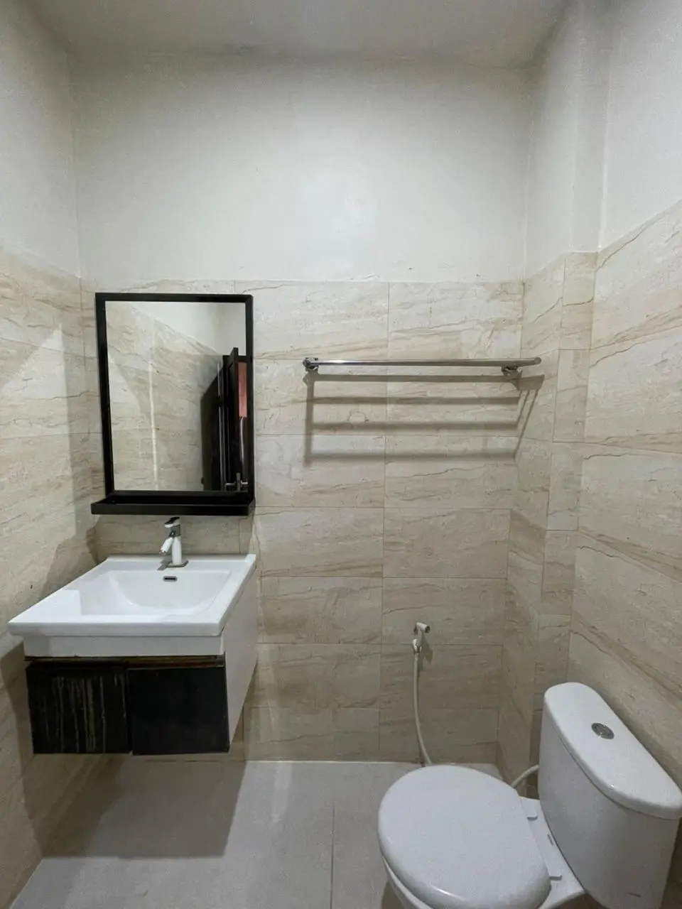Modern hotel bathroom in a deluxe room with a white sink, vanity mirror, and beige tiled walls.