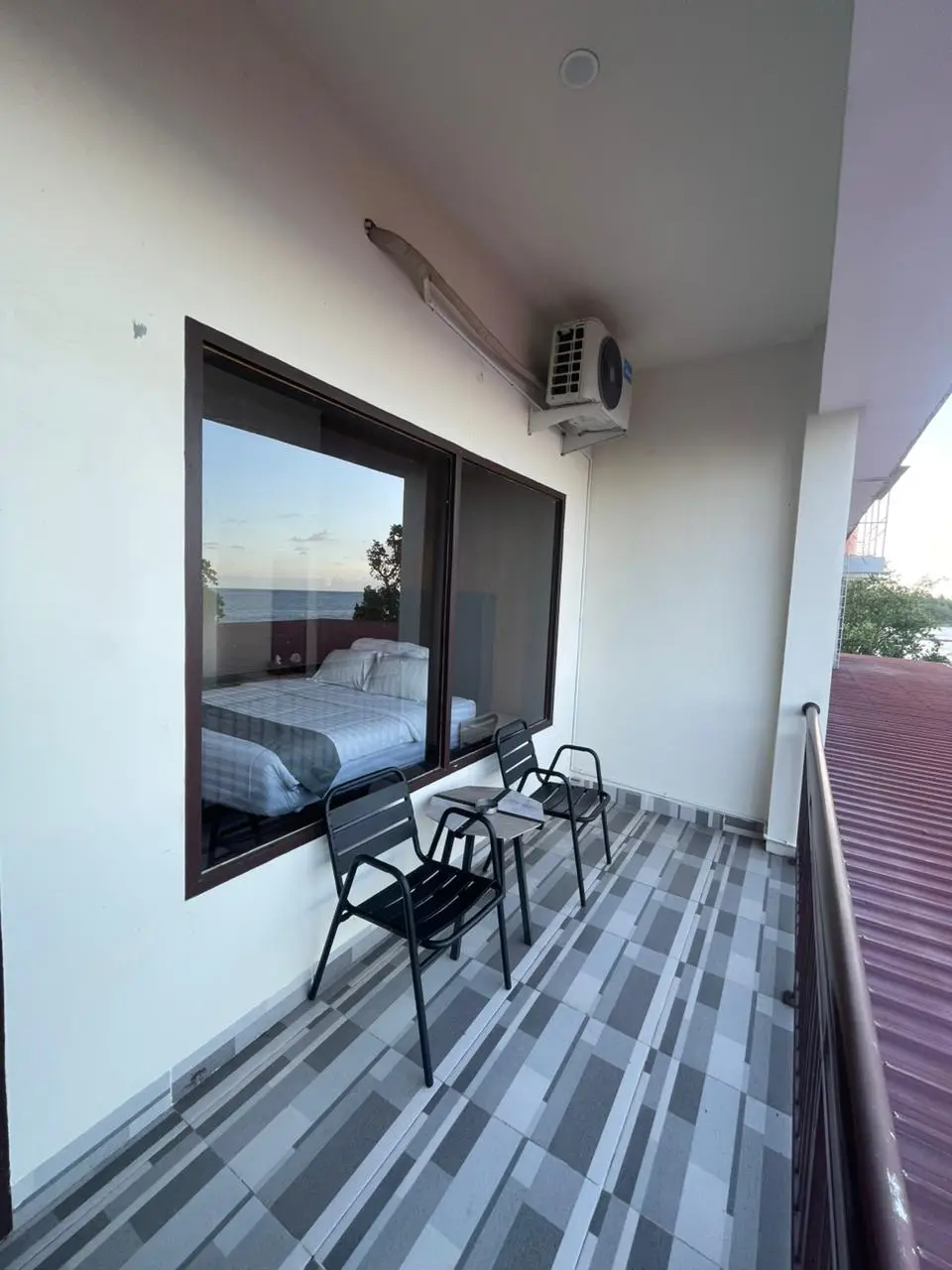 Private balcony of a Deluxe Room with two chairs and a view of the sea reflected in the window.