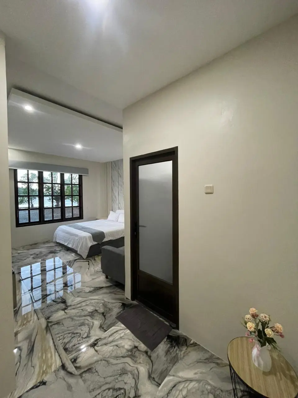 Modern hotel suite with marble-patterned floors, a white double bed, and large windows overlooking a green landscape.
