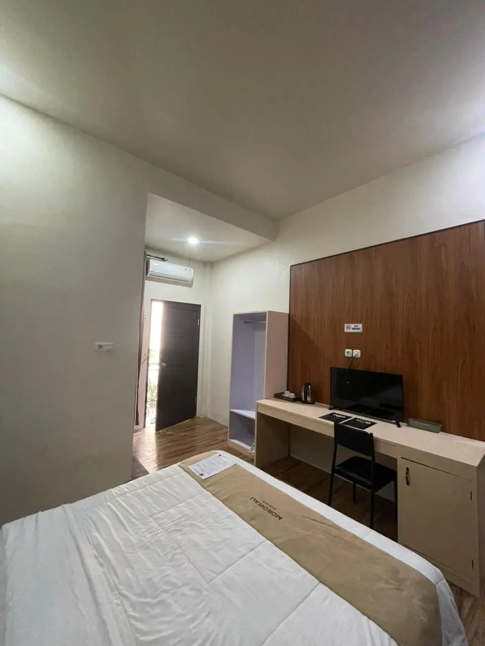 Standard double hotel room with a white bed, a large desk with a TV, and a wood-paneled feature wall.