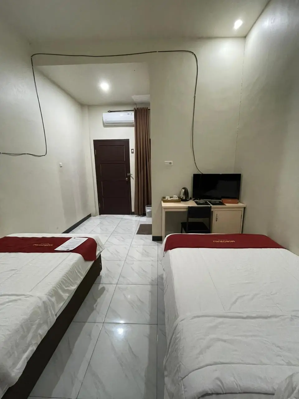Kamar hotel tipe standard twin dengan dua tempat tidur single, runner merah, dan area meja kerja.