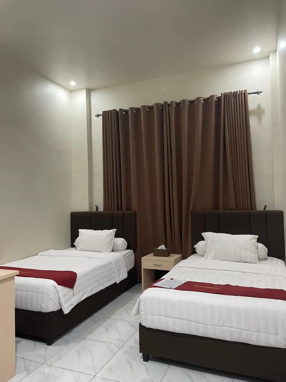 Kamar twin standar dengan dua tempat tidur single, seprai putih, bed runner merah, dan headboard cokelat tua.