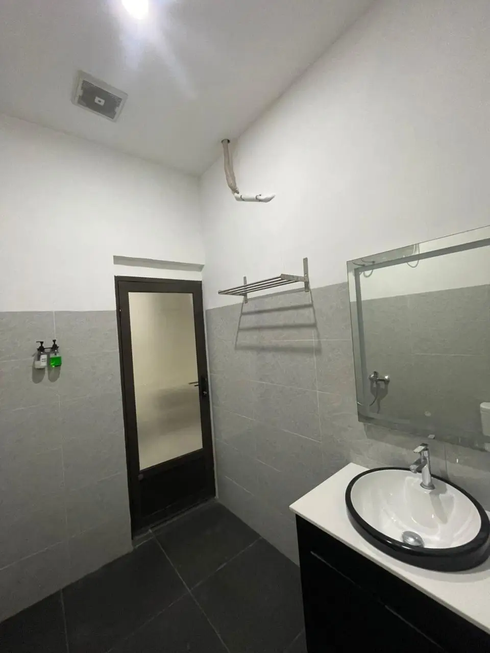 Modern suite room bathroom featuring a white sink with black rim, large mirror, and grey tiled walls.