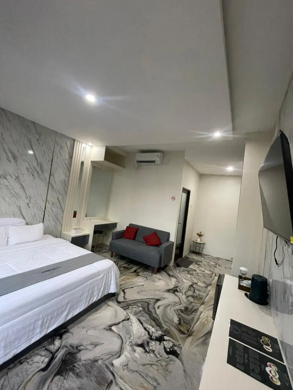 Modern hotel suite featuring a king-sized bed, gray sofa, and a unique marble-patterned floor.