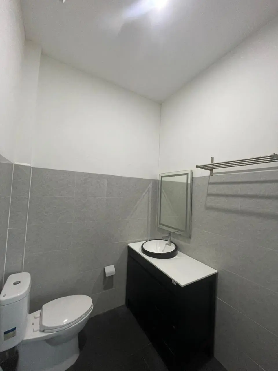 Kamar mandi hotel modern dengan wastafel hitam, bak cuci tangan putih, dan ubin dinding abu-abu.