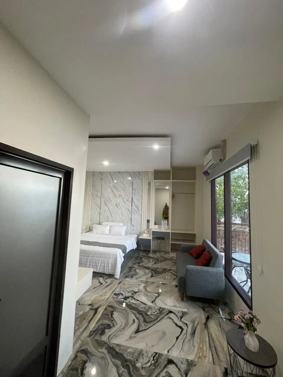 Kamar suite mewah dengan lantai marmer, tempat tidur besar, dan sofa abu-abu di dekat jendela.