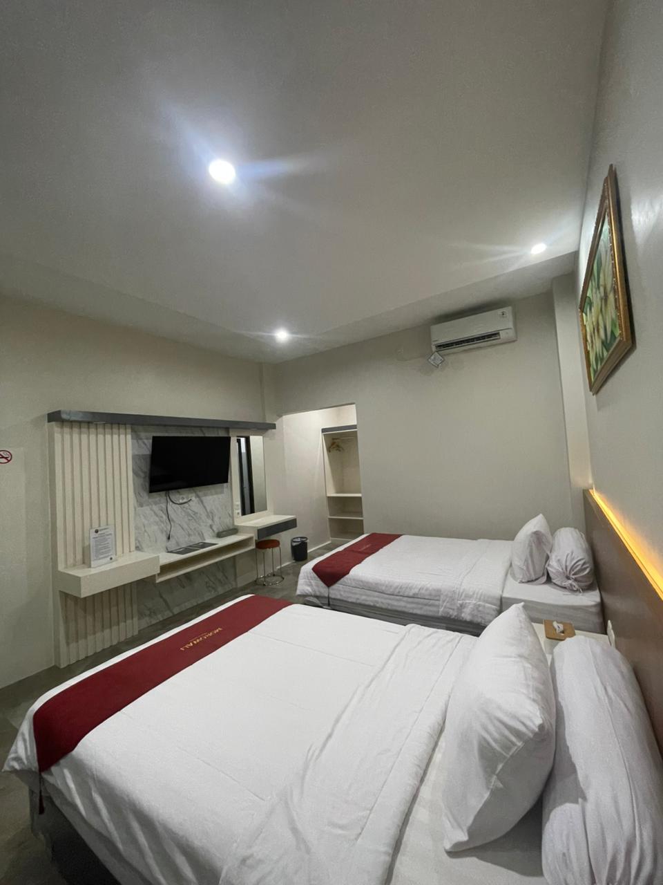 Kamar Junior Suite modern dengan dua tempat tidur double, TV layar datar yang terpasang di dinding, dan dekorasi putih yang bersih.