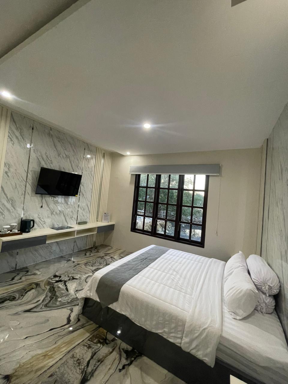 Kamar suite mewah yang menampilkan tekstur dinding dan lantai marmer yang elegan, tempat tidur yang nyaman, dan fasilitas modern.