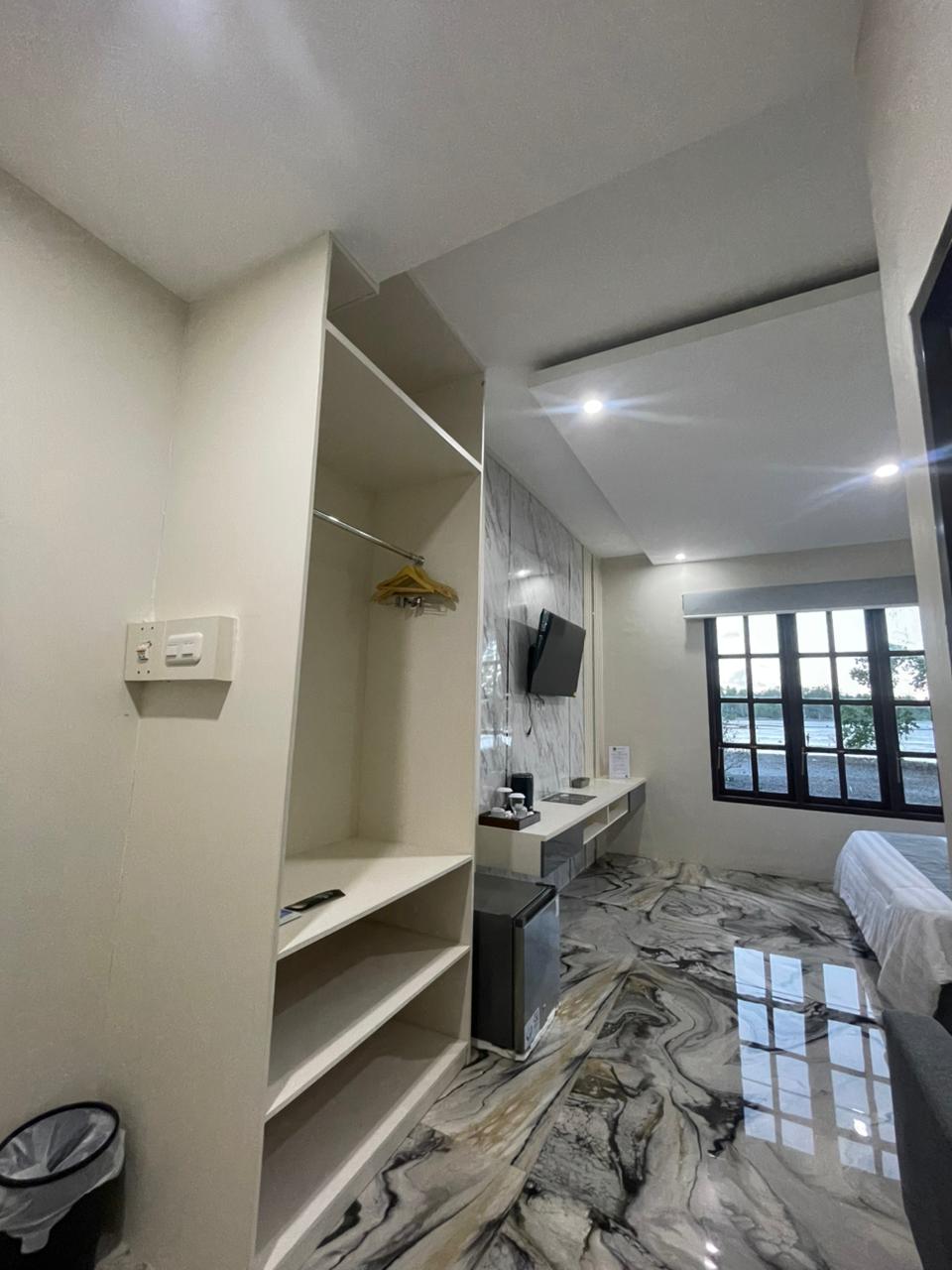 Kamar suite modern dengan lemari terbuka, lantai bermotif marmer, dan TV yang terpasang di dinding.