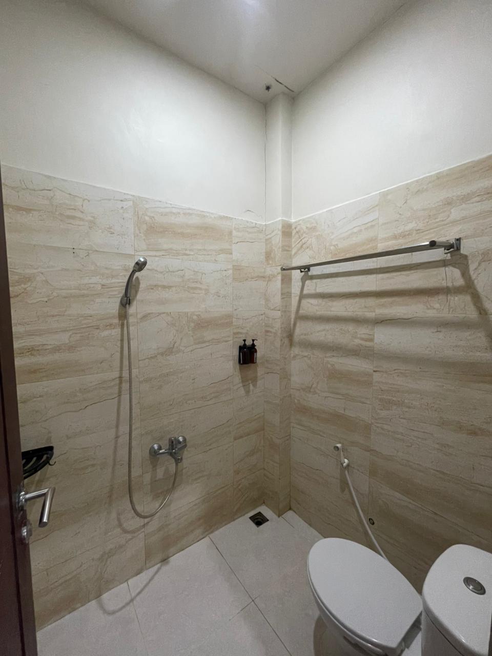 Kamar mandi hotel fungsional di kamar double standar dengan shower dan toilet putih.