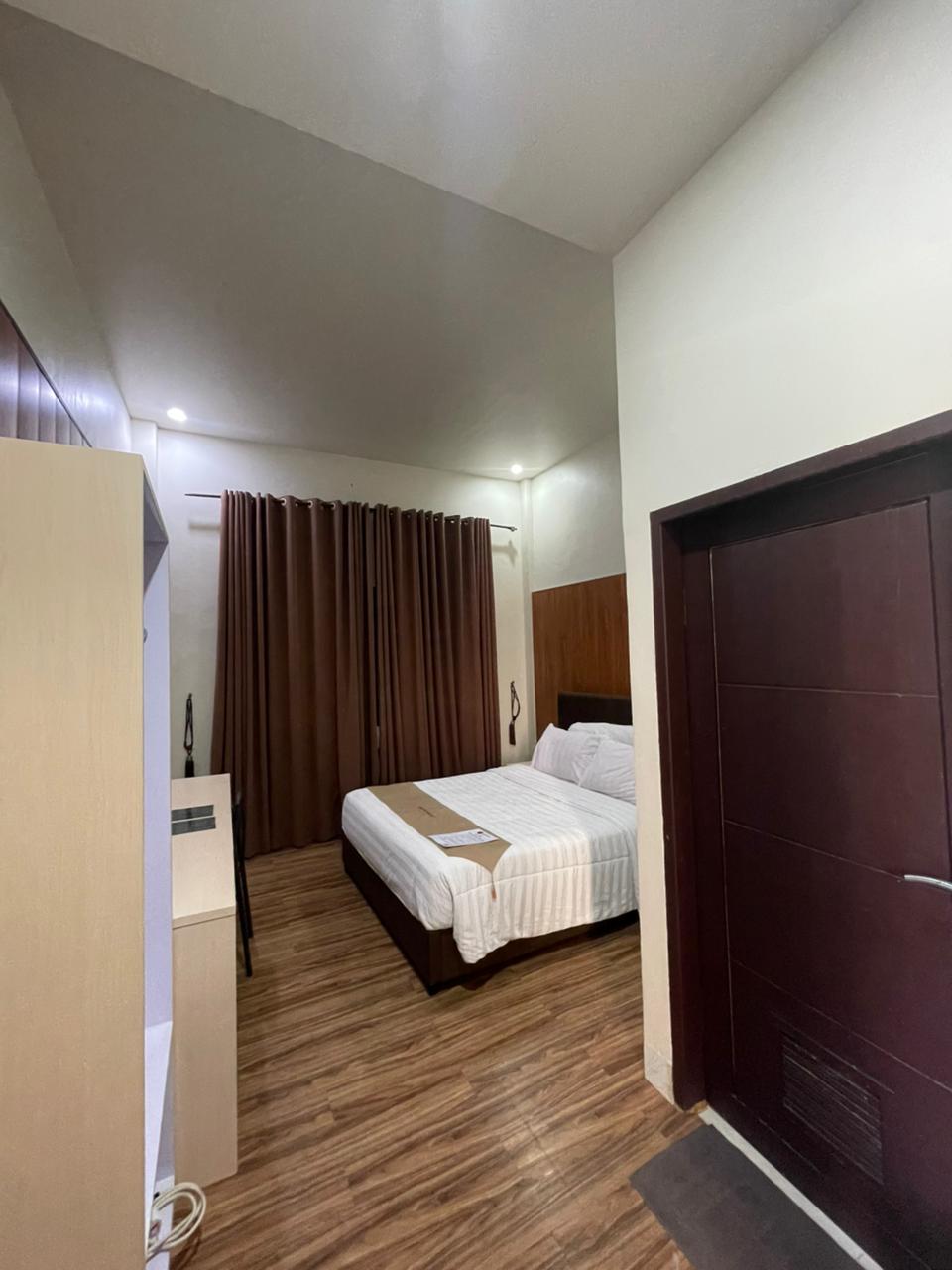 Kamar hotel standar dengan tempat tidur double, tirai cokelat, dan lantai bermotif kayu.