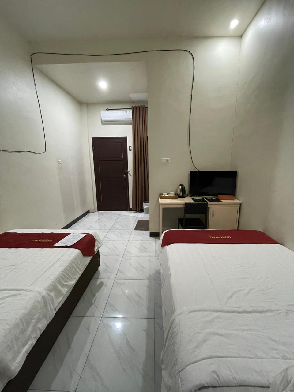 Kamar hotel tipe standard twin dengan dua tempat tidur single, runner merah, dan area meja kerja.