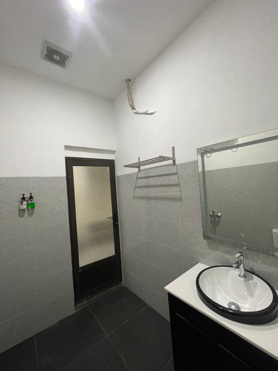 Kamar mandi kamar suite modern dengan wastafel putih bertepi hitam, cermin besar, dan dinding ubin abu-abu.