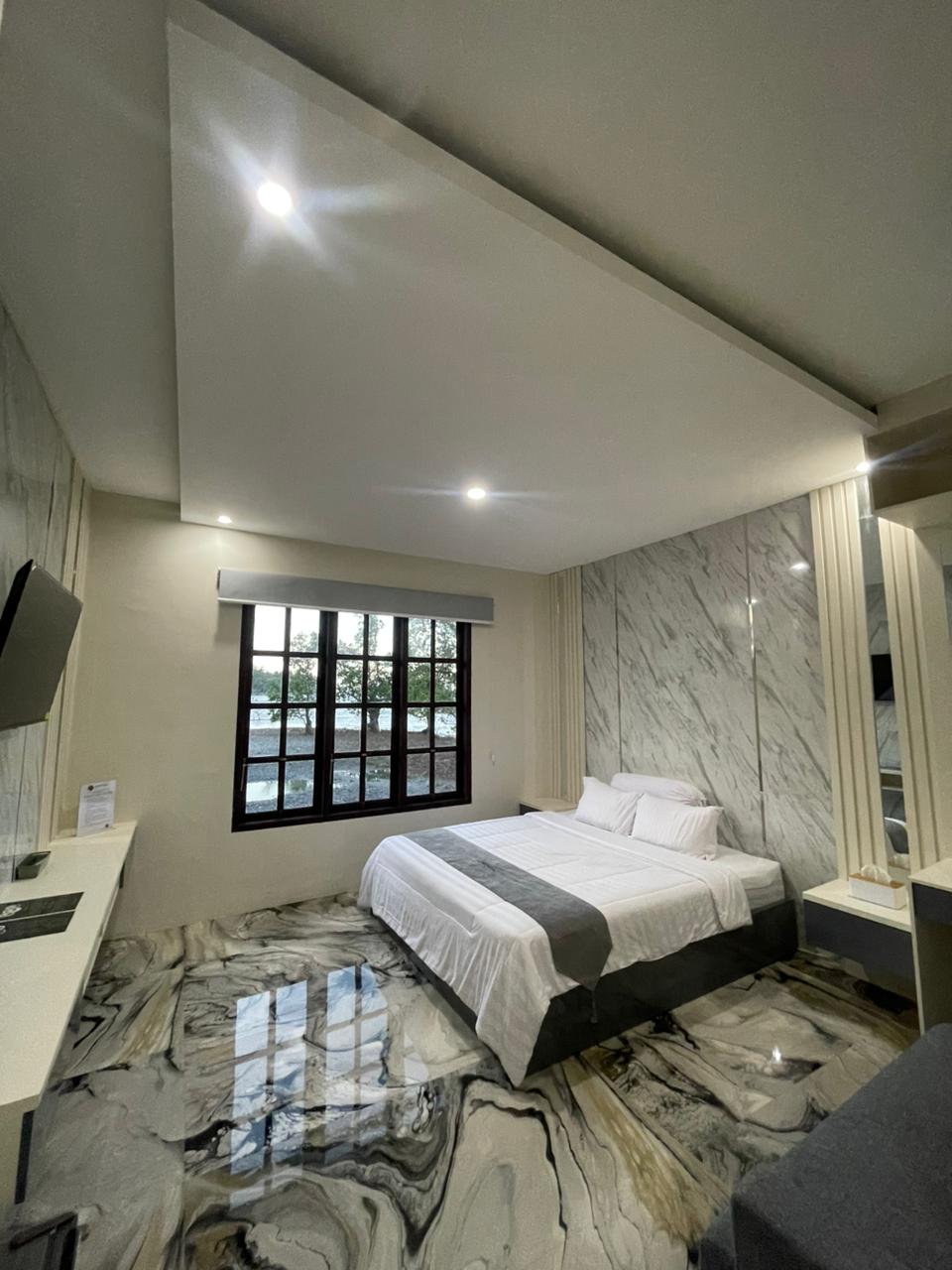 Kamar suite hotel modern dengan lantai bermotif marmer, tempat tidur double dengan seprai putih, dan jendela besar.