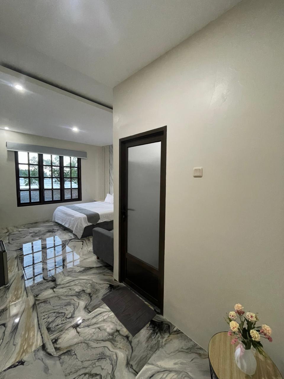Kamar suite modern dengan lantai ubin marmer yang unik, tempat tidur besar dengan seprai putih, dan jendela berbingkai gelap yang menghadap ke pepohonan.
