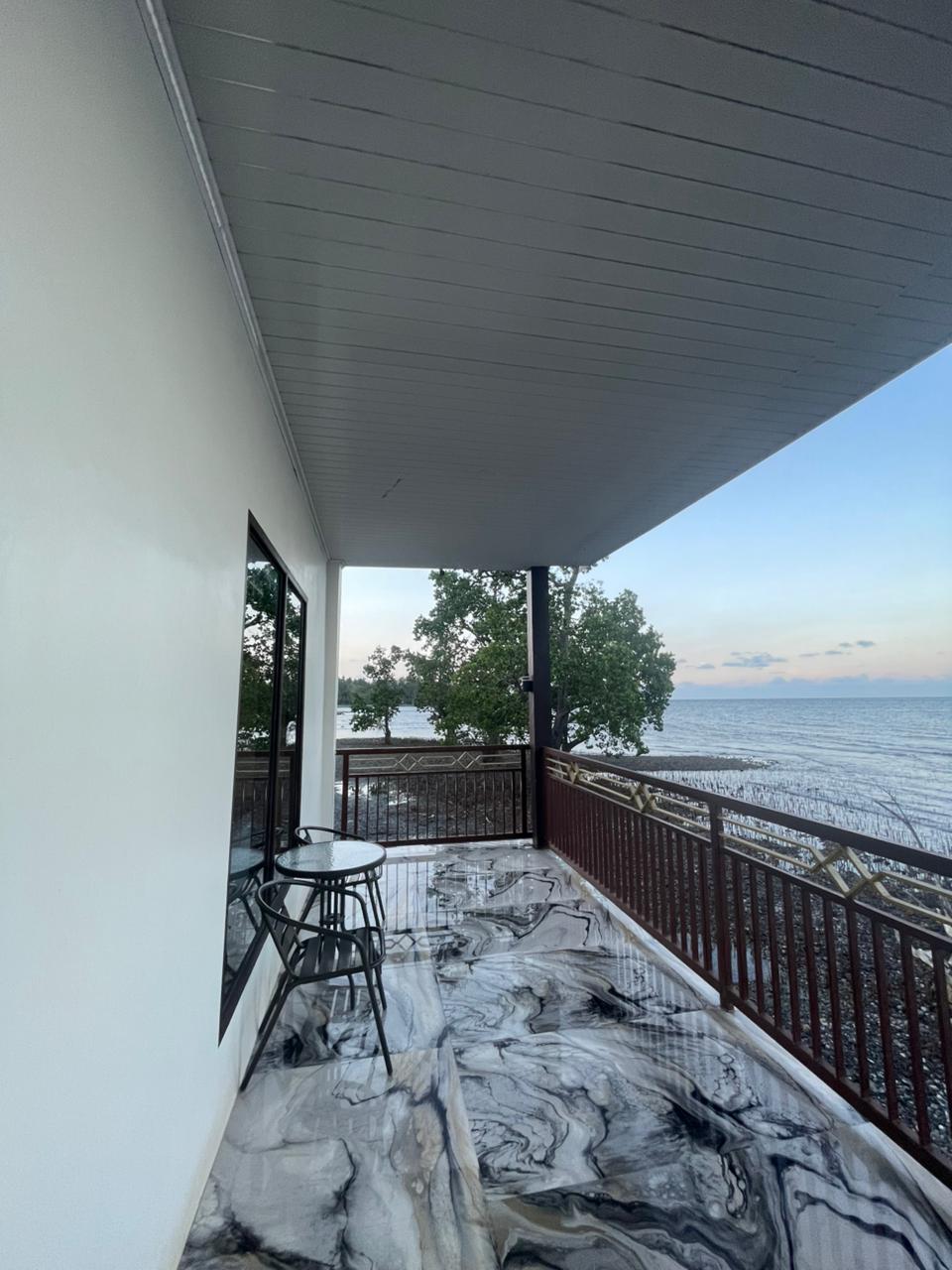 Balkon pribadi di kamar suite dengan lantai bermotif marmer dan pemandangan laut yang indah saat senja.