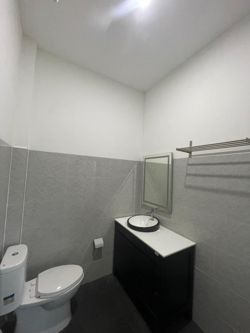 Kamar mandi hotel modern dengan wastafel hitam, bak cuci tangan putih, dan ubin dinding abu-abu.