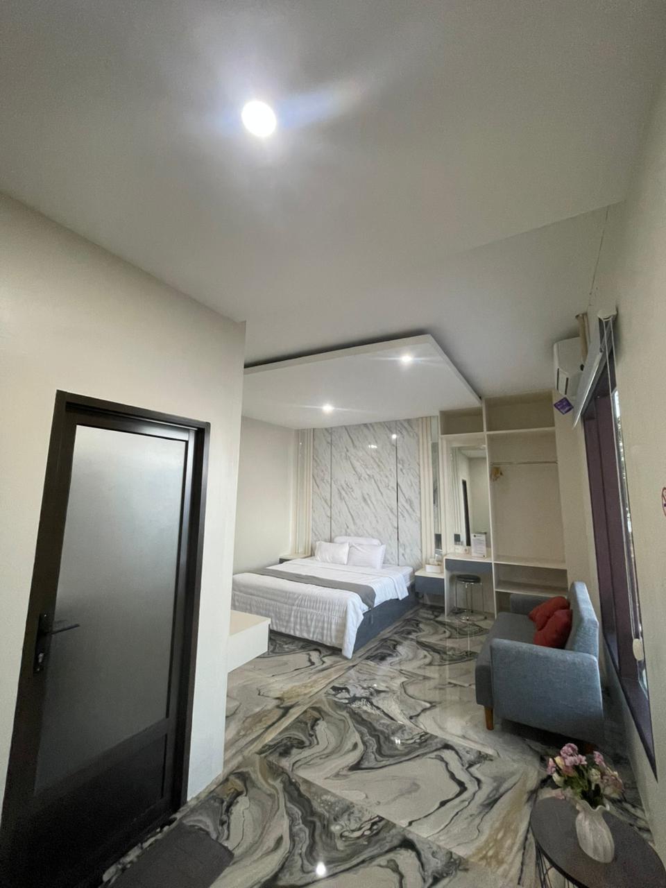 Kamar tipe suite modern dengan tempat tidur putih, sofa abu-abu, dan lantai bermotif marmer yang unik.